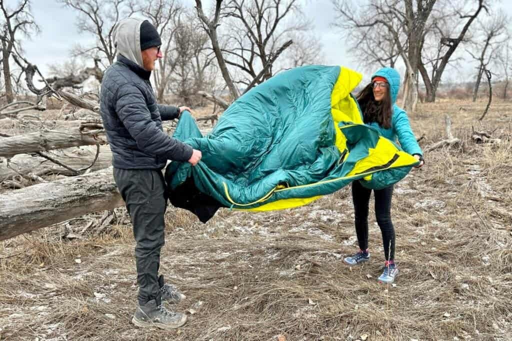 A couple is folding and putting away a winter double sleeping bag.