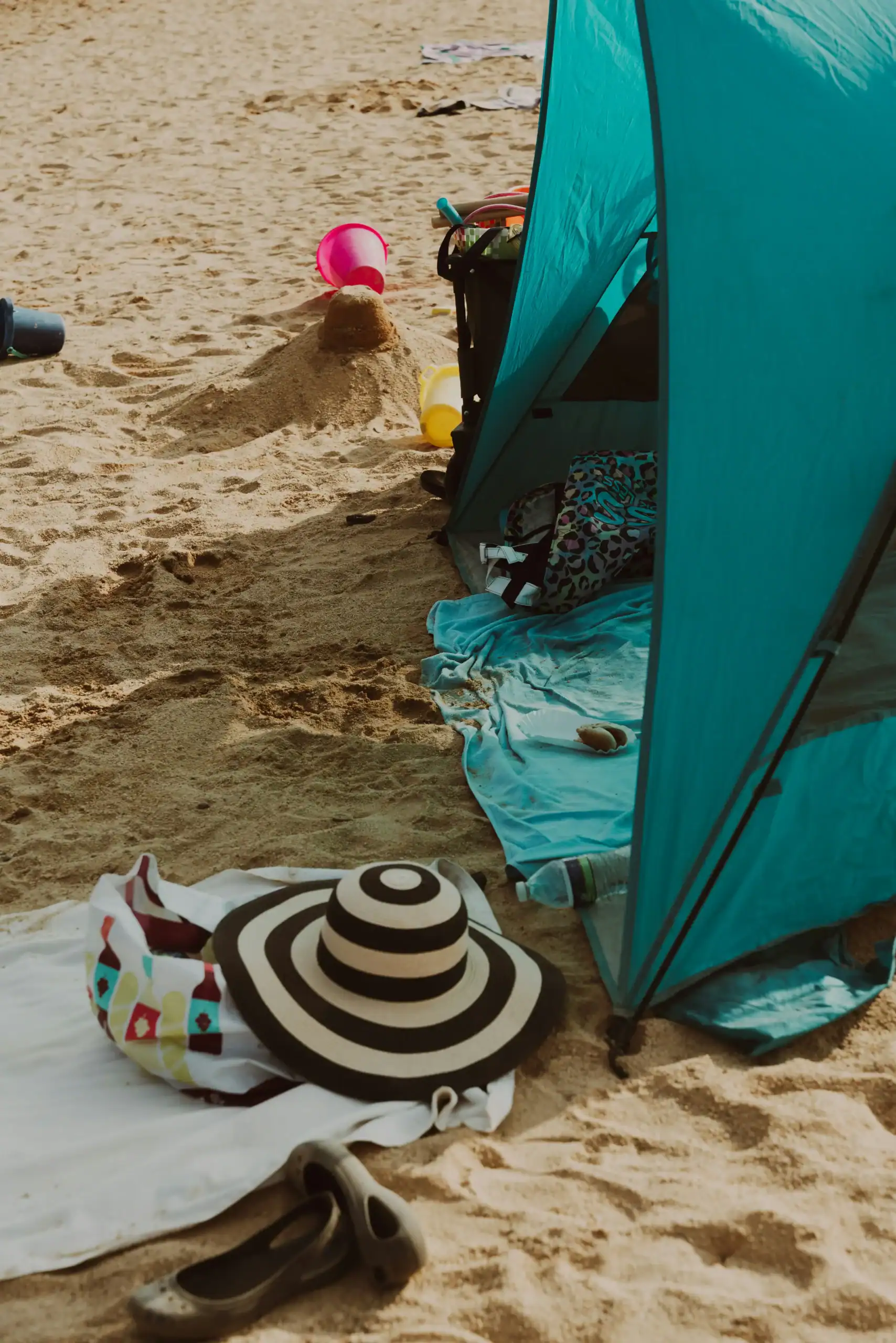 Beach Tent vs. Wind: Anchoring Solutions for Rental Fleets 2 Beach camping scene with tent, toys, and accessories on sandy shore.