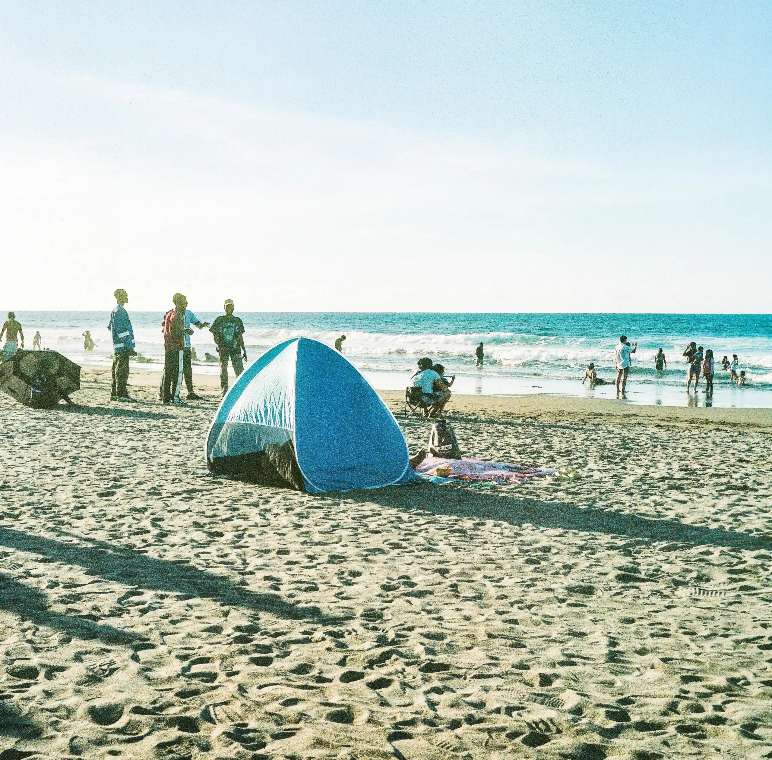 Beach camping with a blue tent on sandy shore during daytime.