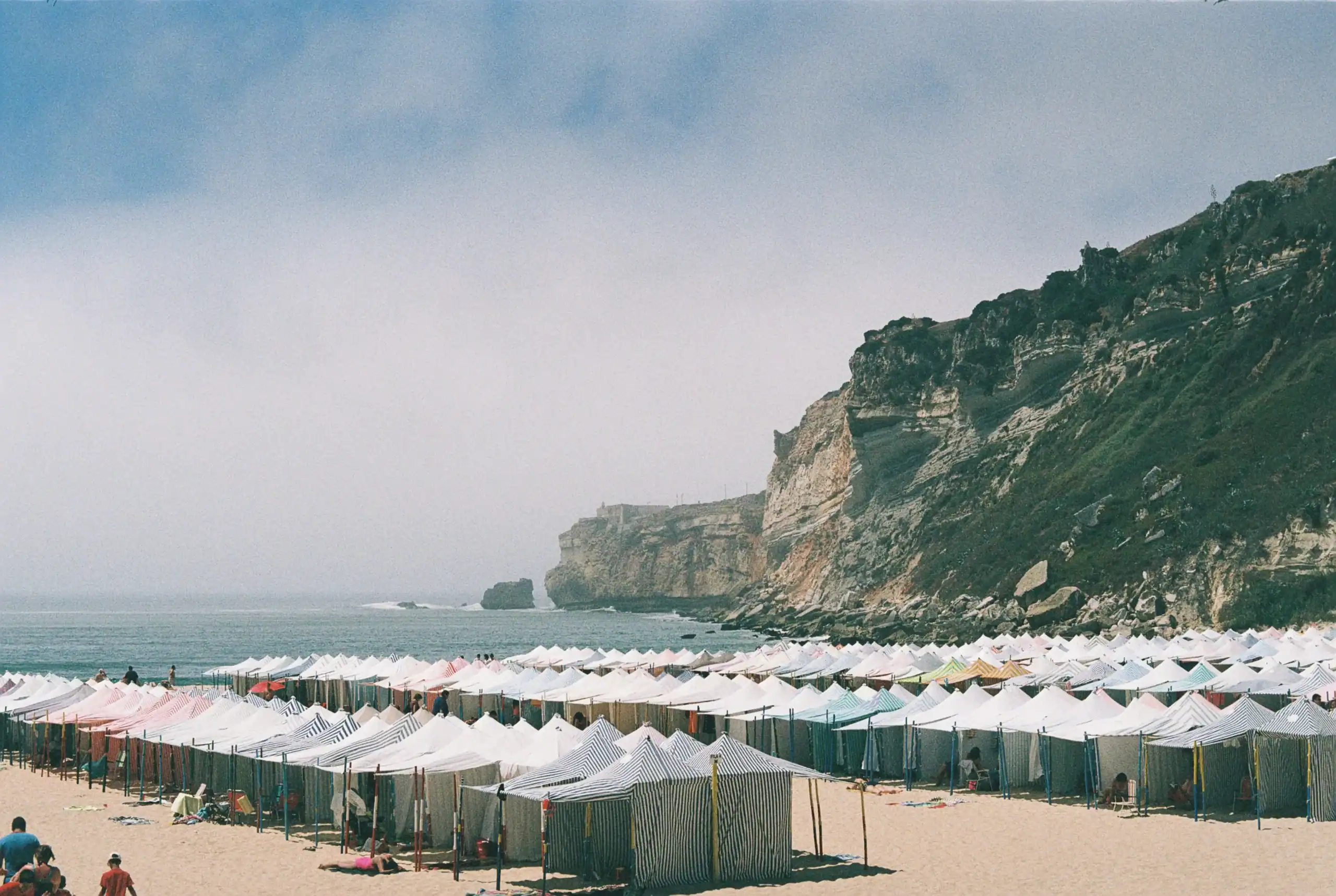 Beach camping tents along the shoreline with cliffs in the background.