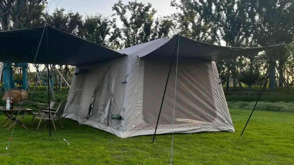 هل تستحق الخيام القابلة للنفخ في عام 2026؟ الإيجابيات والسلبيات والأساطير 3 خيمة تخييم كبيرة مع مظلة مرفقة وأثاث خارجي وحقل أخضر تحت الأشجار في الخلفية