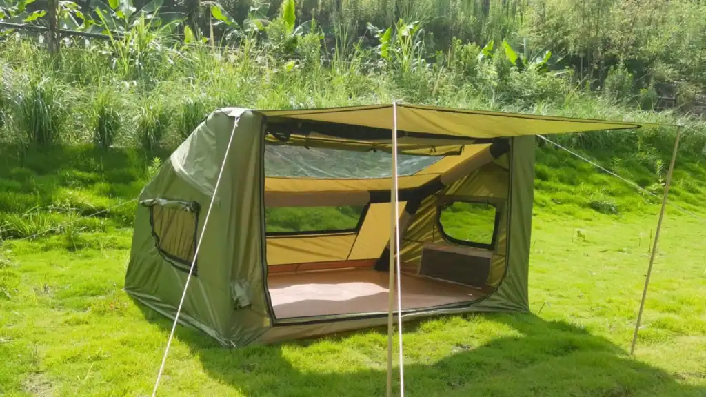 Green outdoor camping tent with large mesh windows and extended canopy set up in grassy area