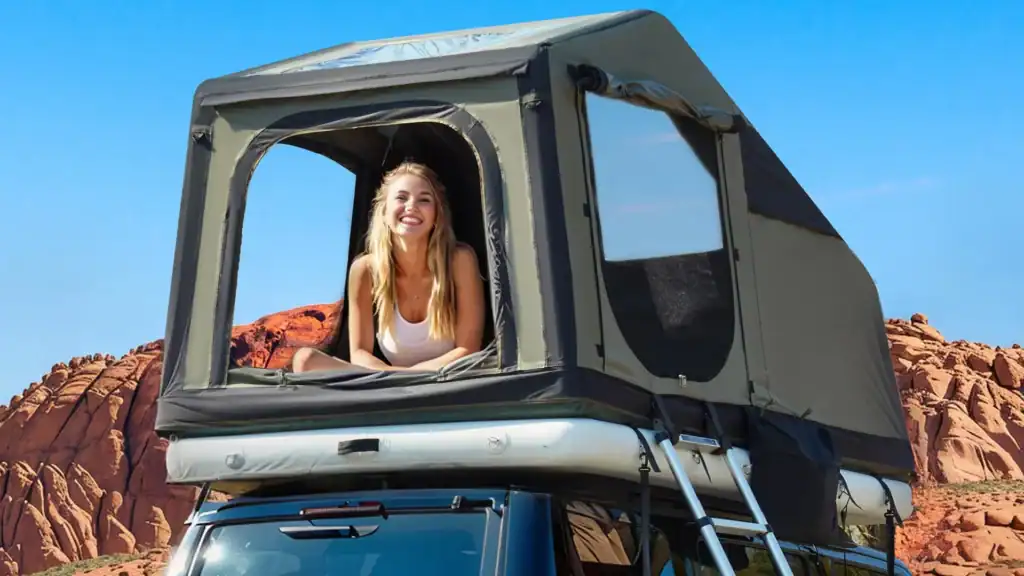 Woman smiling in a rooftop tent during outdoor camping in a desert landscape.