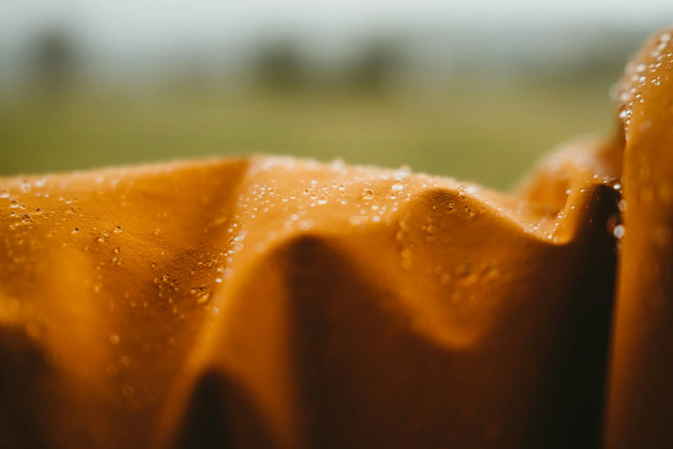 Close-up of water droplets on outdoor fabric with blurred natural background.