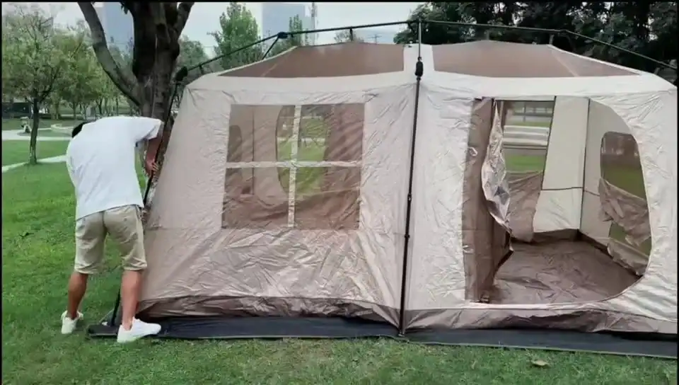 Outdoor camping tent with open doors and windows in a park setting.