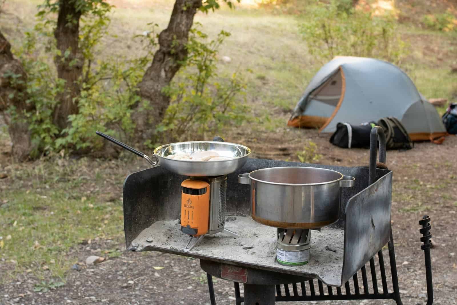 Outdoor camping stove and cookware in a forest setting.