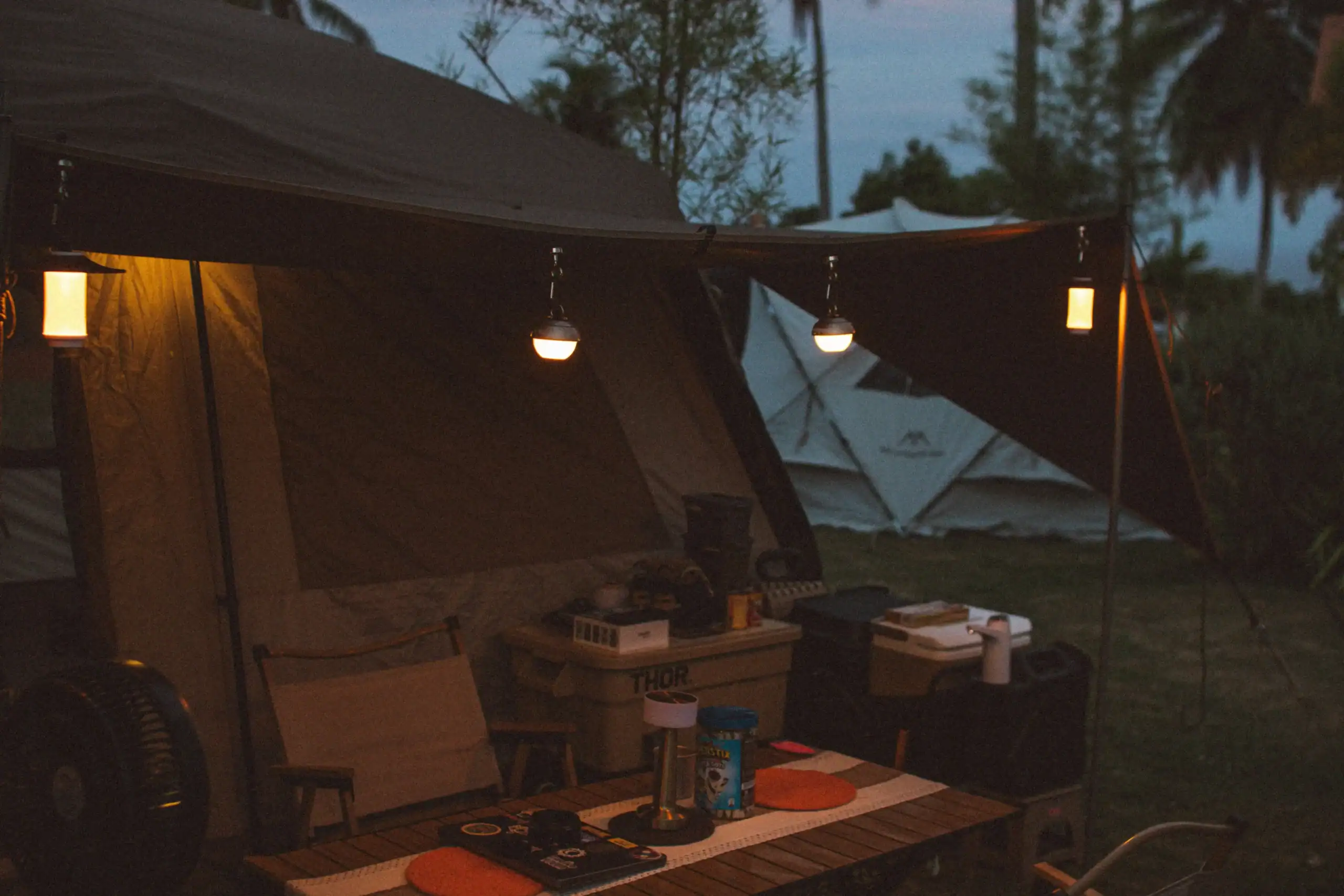 Montagem de barraca de camping com iluminação quente e equipamentos para atividades ao ar livre.