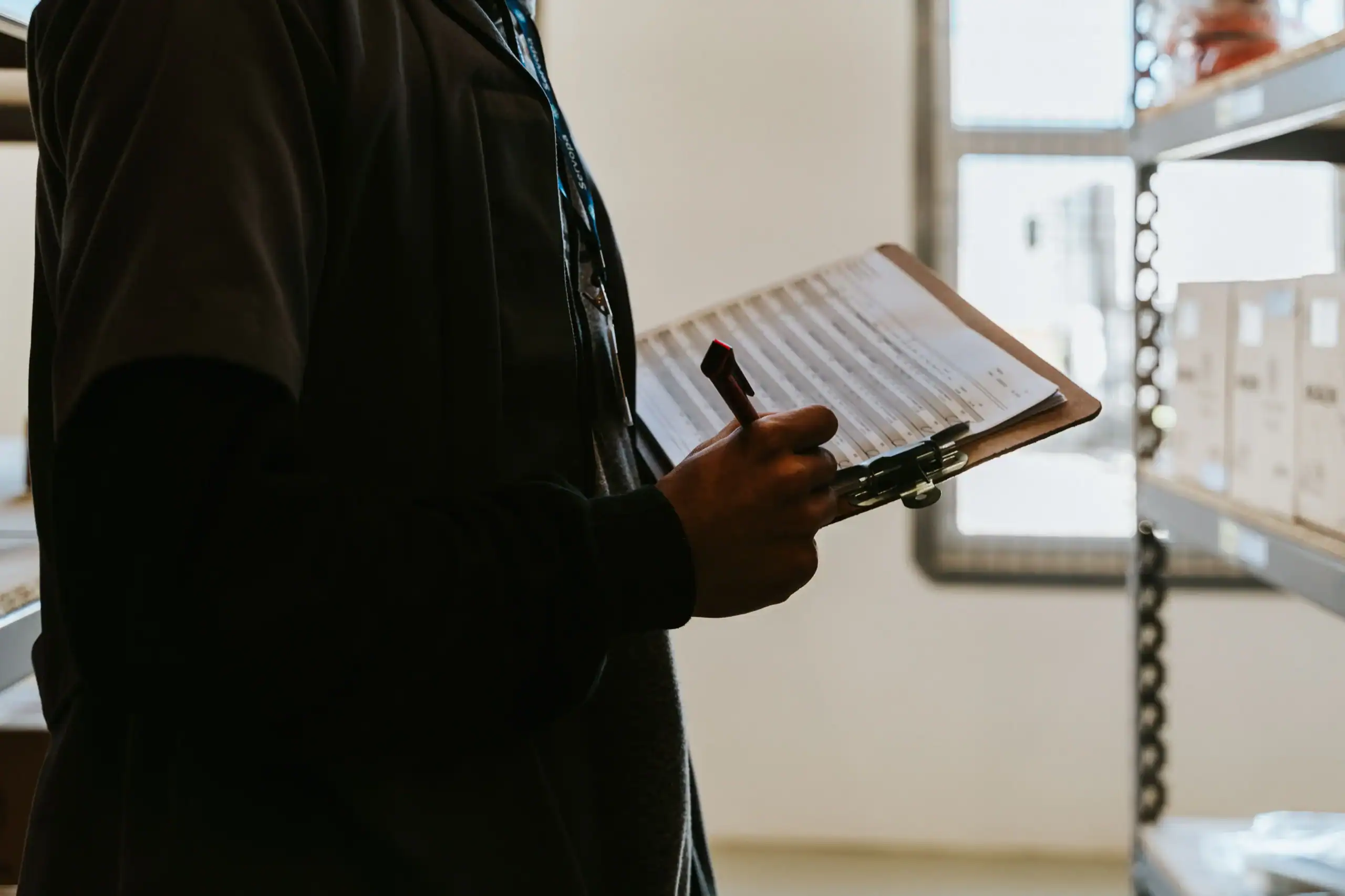 Person holding a clipboard in a storage room, managing outdoor equipment inventory.