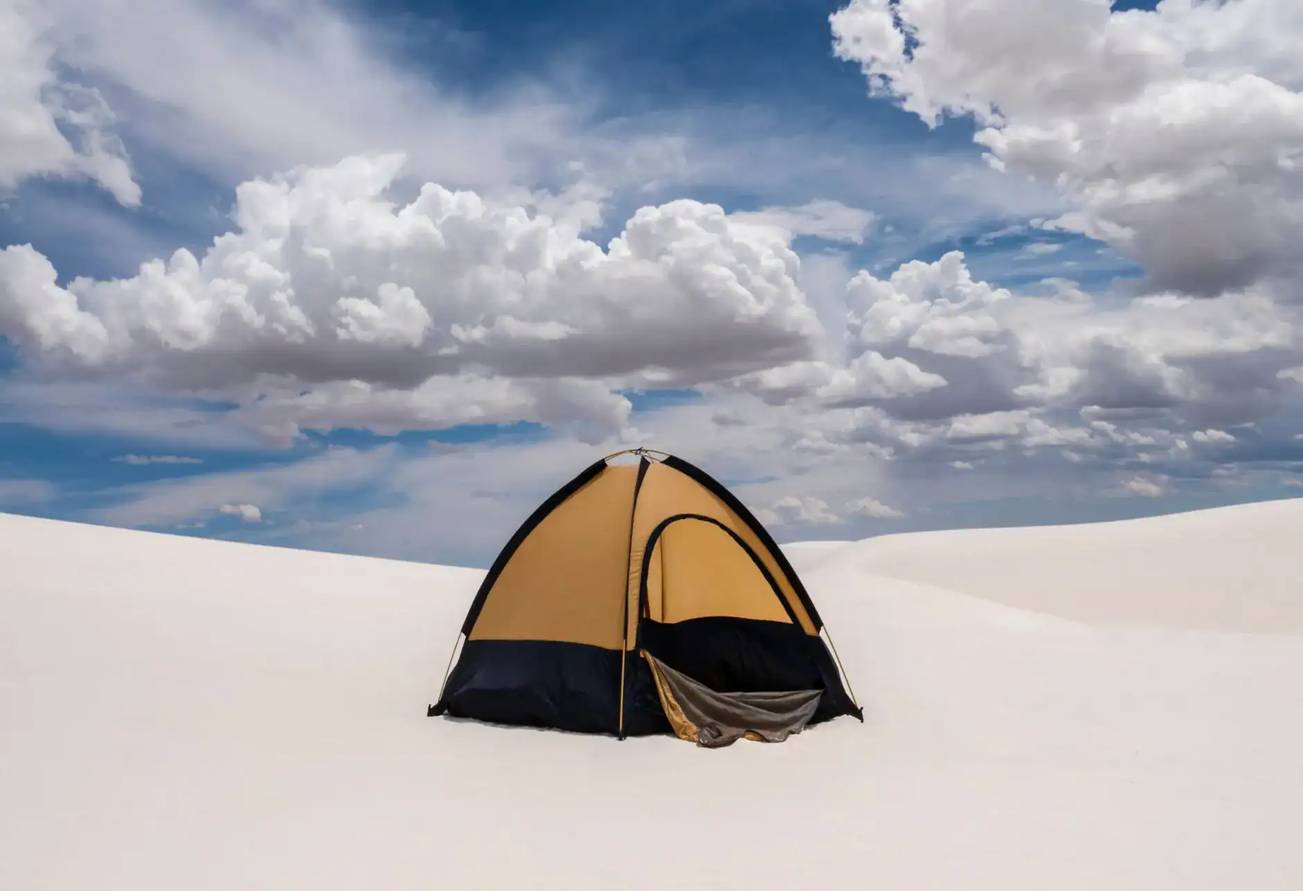 Camping tent in white sand desert with dramatic clouds overhead.