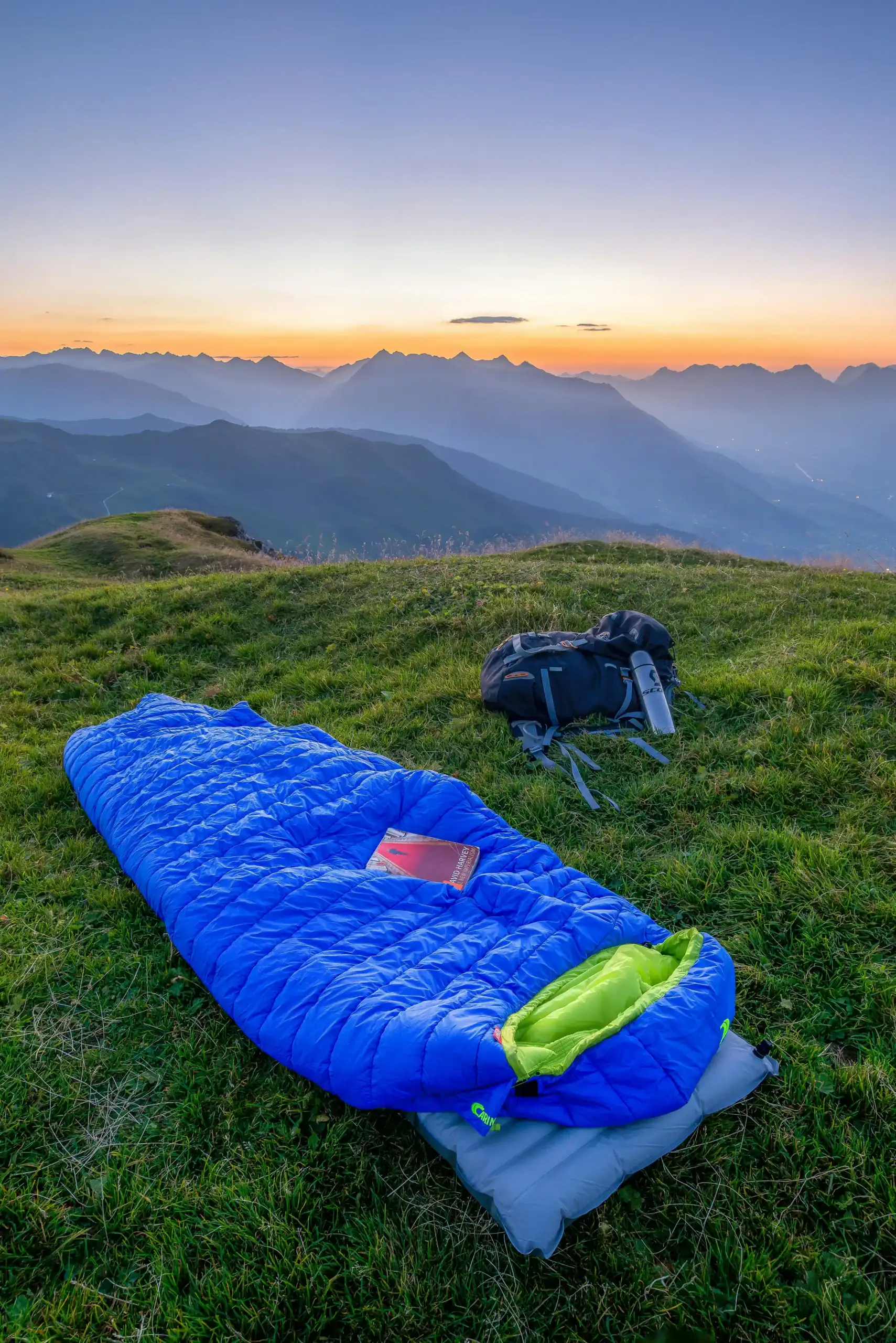 Sleeping Bags Under 1kg: Test Results & Engineering Insights 6 Equipamento de acampamento em um topo de colina gramado com vistas das montanhas ao pôr do sol.