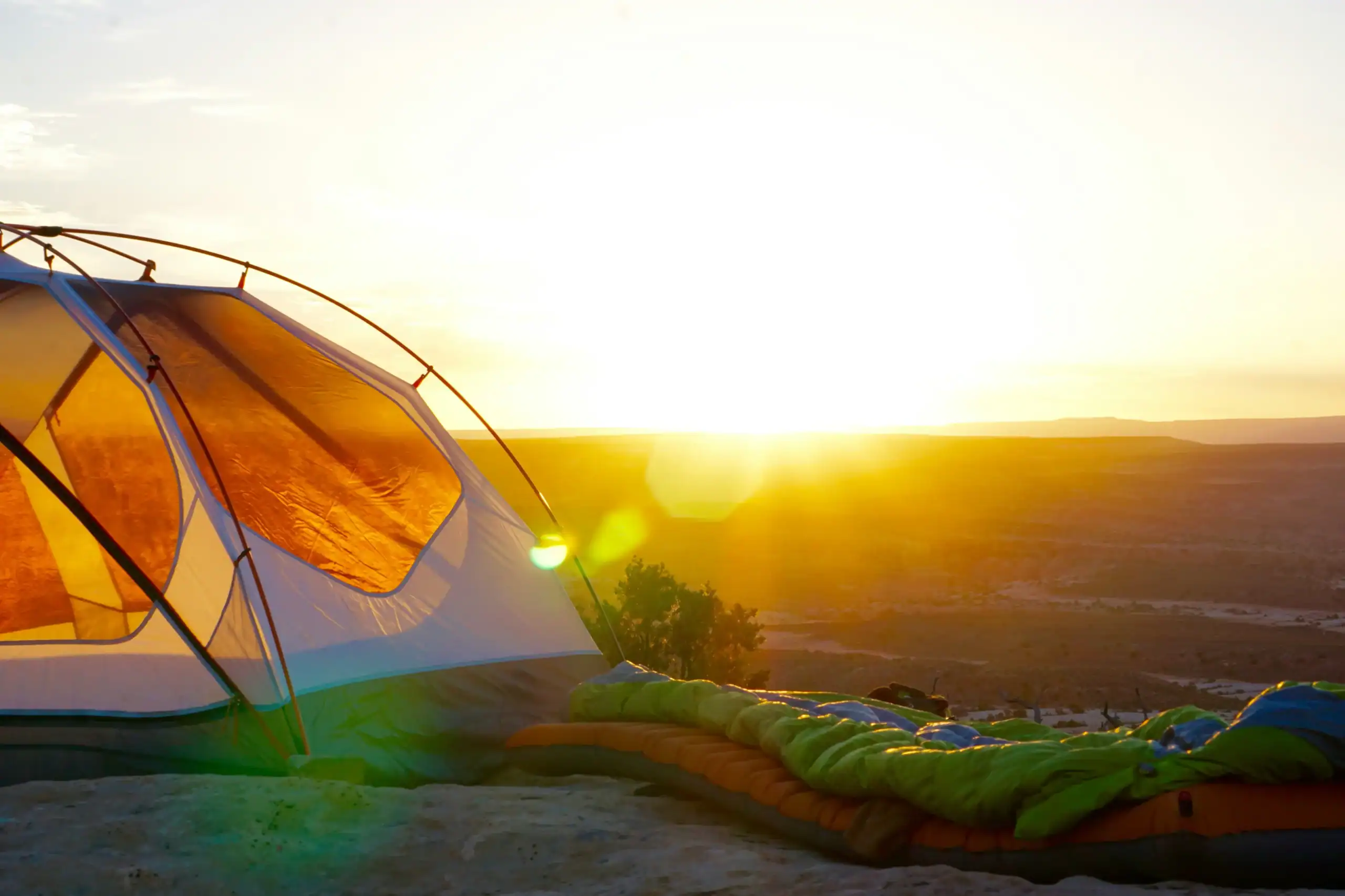 Outdoor camping tent set up during sunset with a sleeping bag nearby, showcasing a peaceful wilderne.