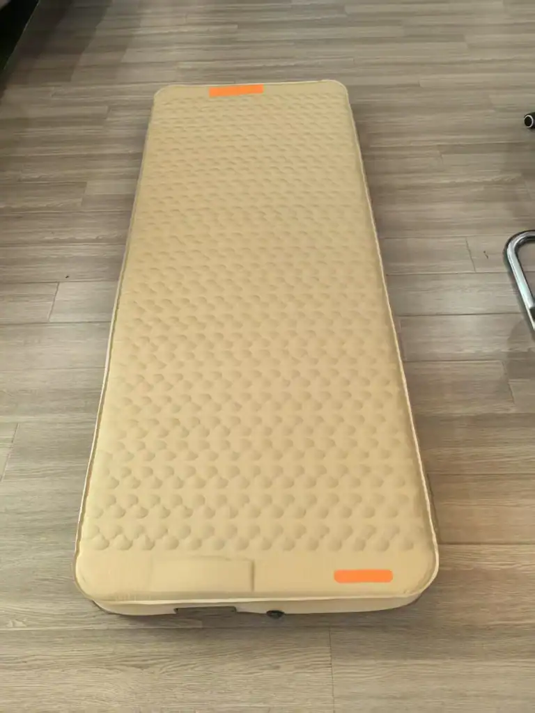 Air Mattress Leaks: 5 Hidden Weld Failures & Fixes 2 Однотонный бежевый надувной матрас на деревянном полу с оранжевыми бирками.