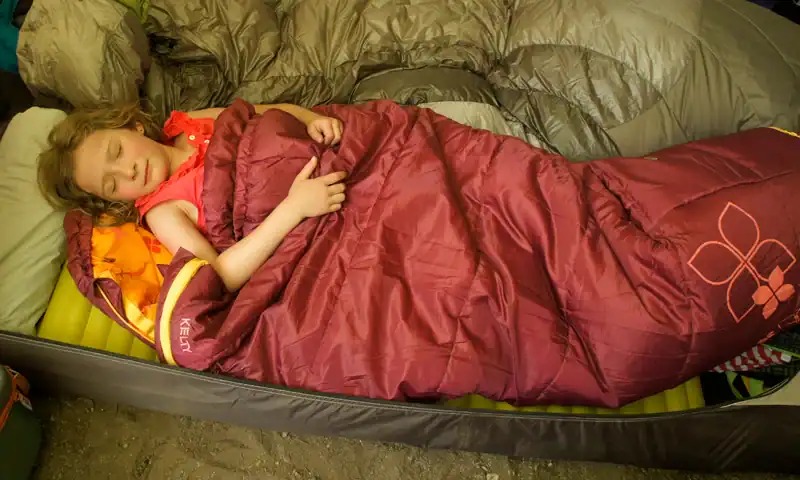 Guia de Compra de Saco de Dormir de 1 kg: 5 Verdades Críticas Sobre Peso 4 Menina jovem dormindo em um saco de dormir dentro de uma barraca durante camping ao ar livre.