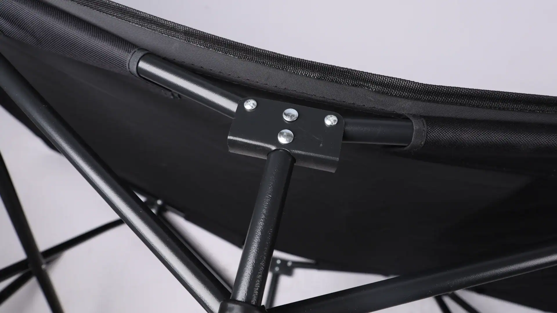 Detailed view of a folding chair's black fabric and sturdy metal frame with securely fastened bolts on a light background.