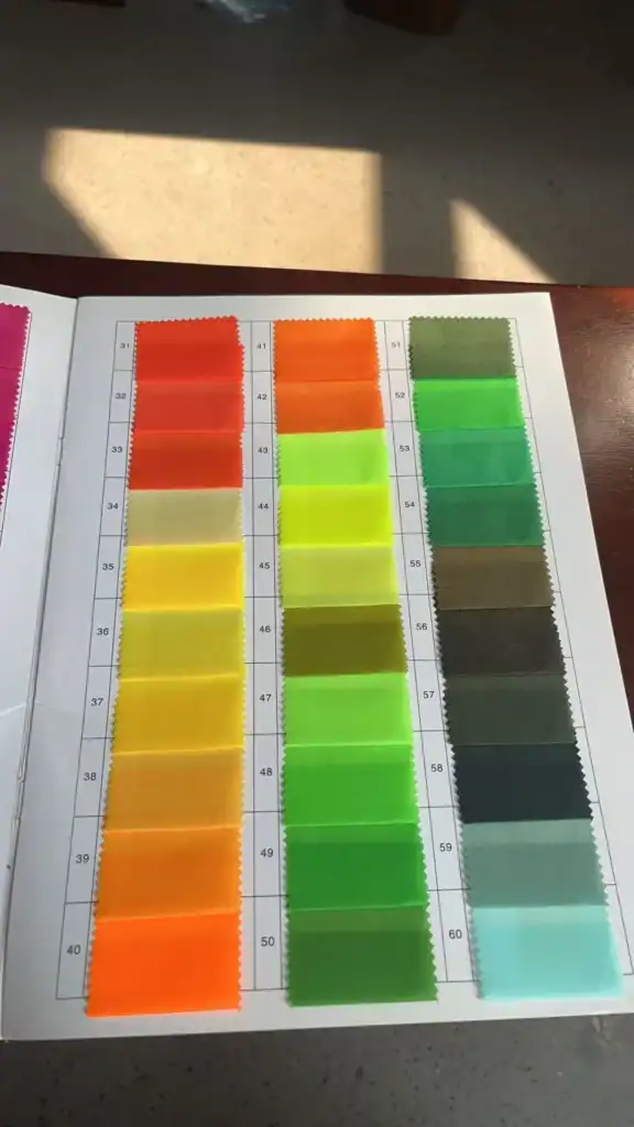 An open book displaying fabric swatches in a grid, with gradient colors ranging from orange to green and blue hues under natural lighting.