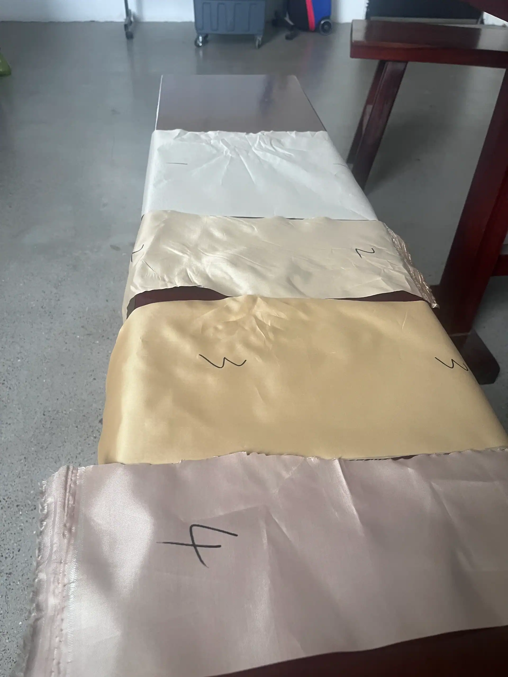 Cuatro muestras de tela en tonos blanco, beige, dorado y rosa, numeradas, dispuestas sobre una mesa de madera en una habitación bien iluminada.