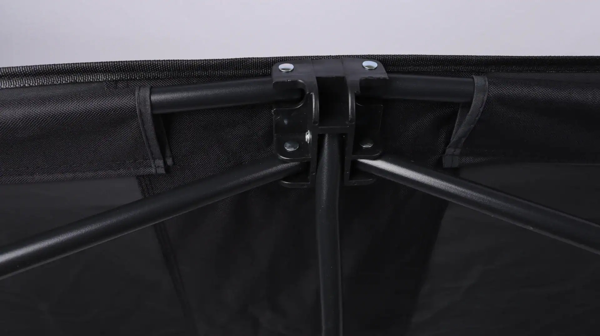 Folding Wagon Weight Limits: Static vs Dynamic Capacity 16 Detail of black folding camping gear frame with sturdy metal connections and reinforced fabric tarp on a light background.