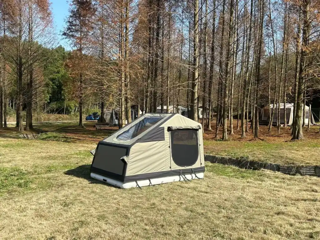 Portable camping tent set up in a forest clearing with trees and tents in background.