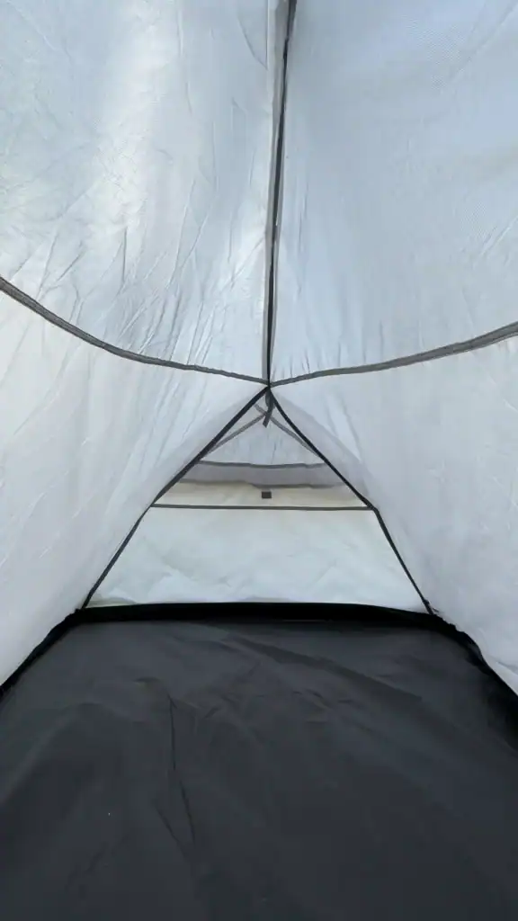 Interior view of a camping tent showing its spacious design with white mesh walls, a triangular vent, and a black floor.