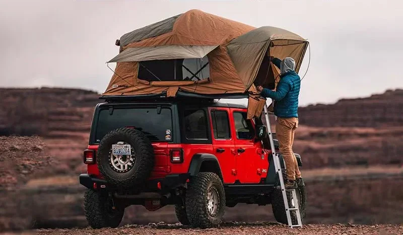 Veículo off-road vermelho com tenda no teto em uma paisagem desértica.