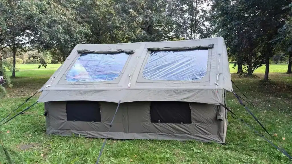 Large outdoor camping tent set up in a grassy park with trees in the background.