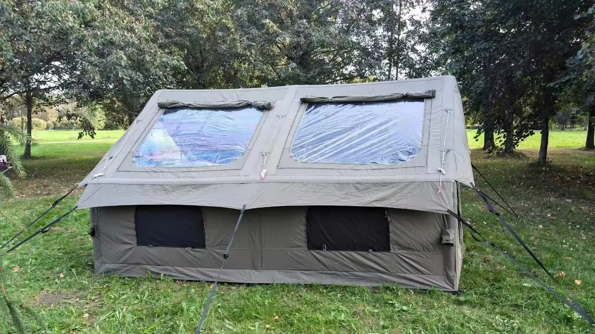 Large outdoor camping tent set up in a grassy park with trees in the background.