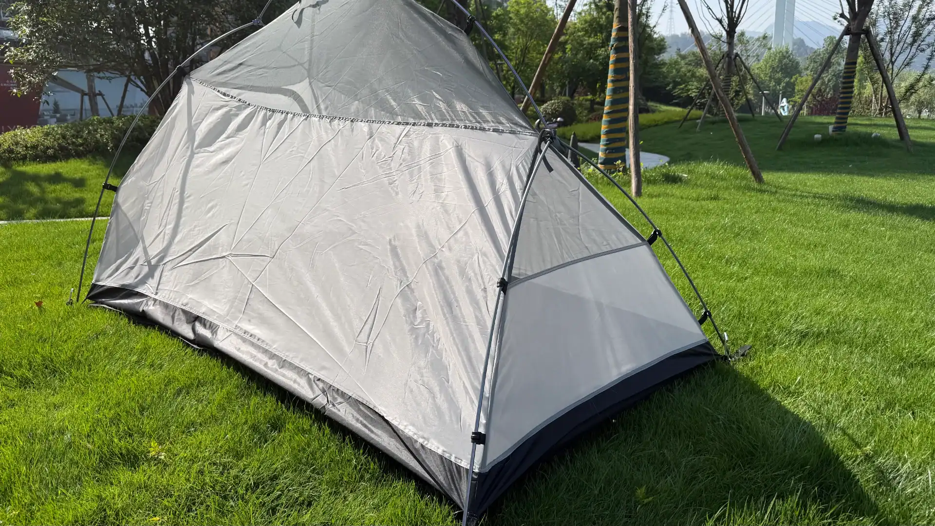 Ein leichtes Campingzelt mit schlankem Design, auf einer grünen Grasfläche unter sonnigem Wetter aufgebaut, umgeben von Bäumen.