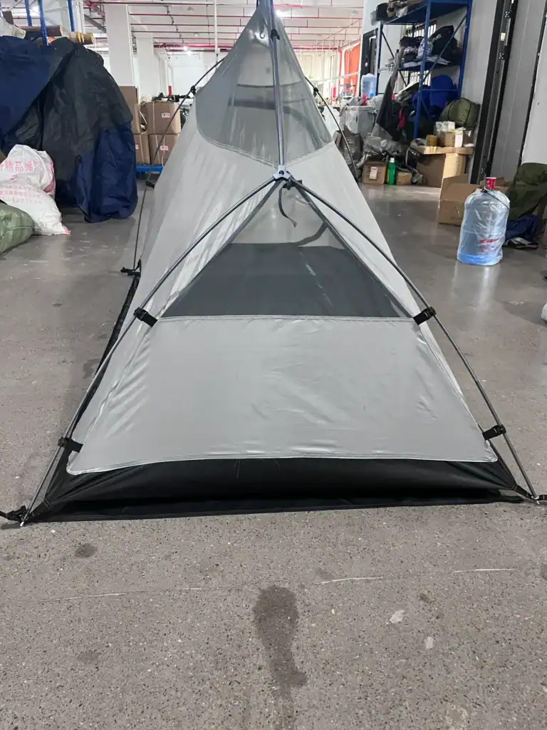 Single-person lightweight gray camping tent with mesh panels, set up indoors on a concrete floor in a warehouse setting.