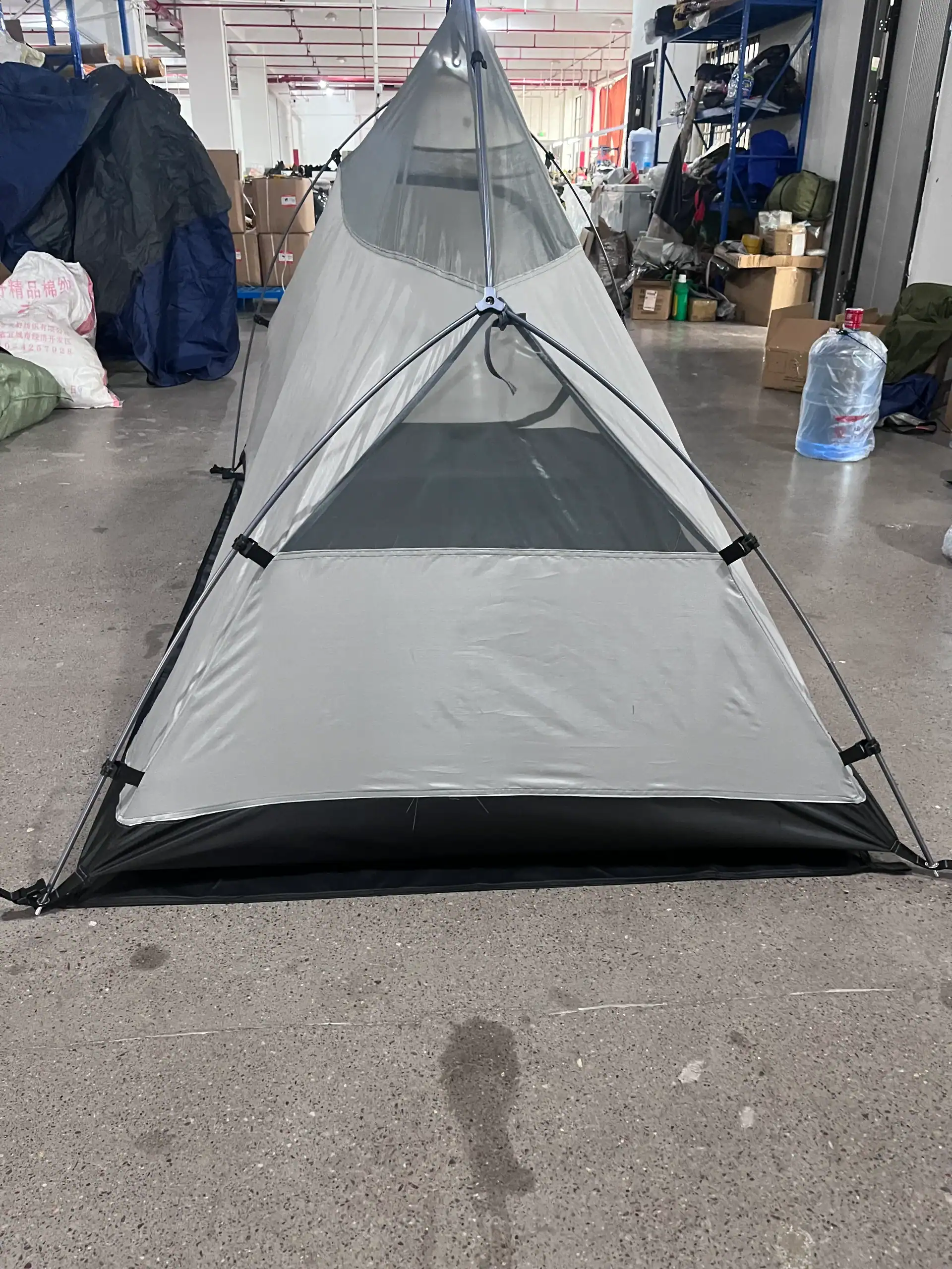 Single-person lightweight gray camping tent with mesh panels, set up indoors on a concrete floor in a warehouse setting.