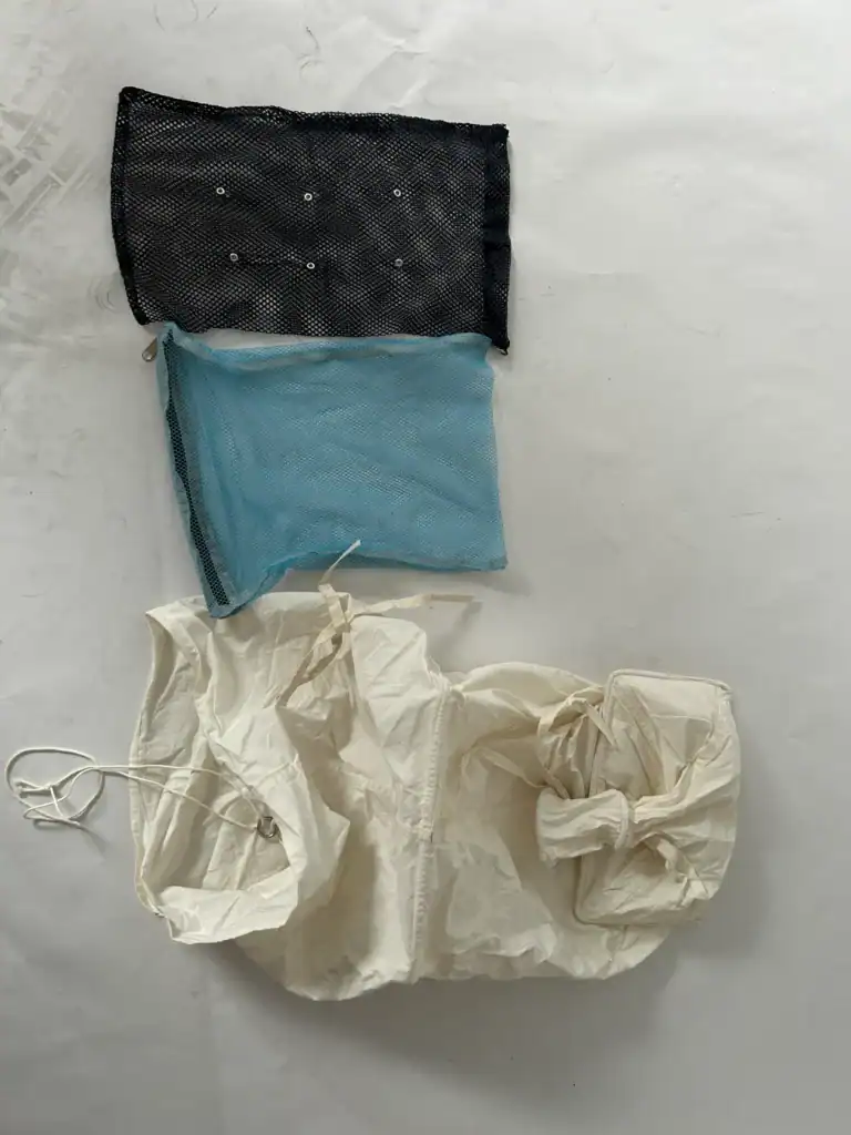 Three different materials: a black mesh pouch, a blue mesh pouch, and a white fabric with strings, displayed on a white surface.