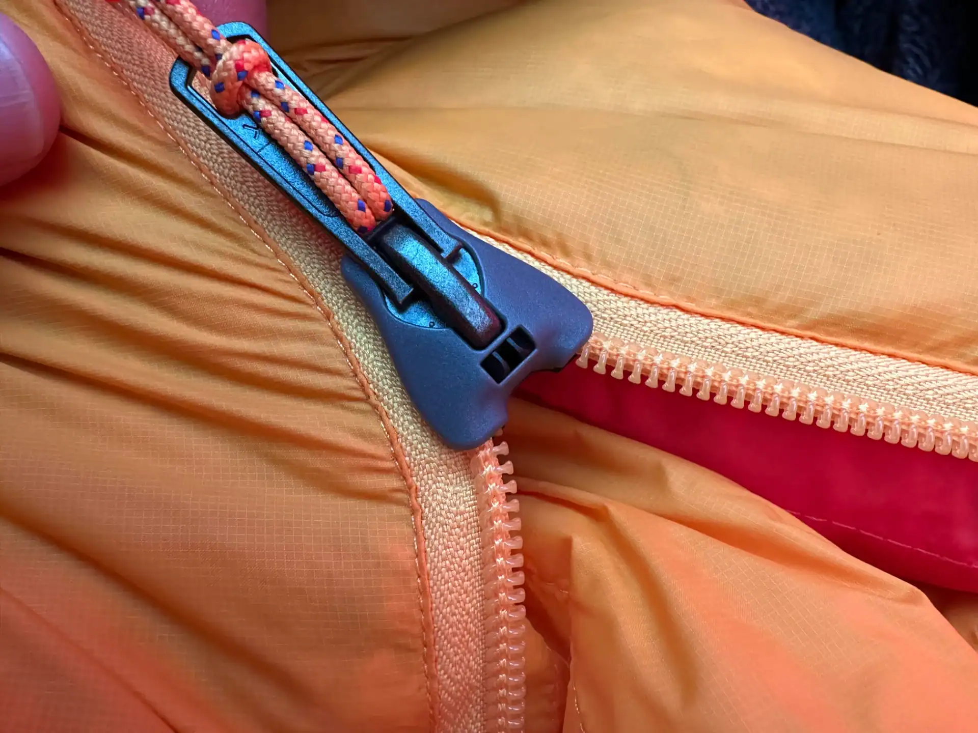 Close-up of orange outdoor jacket with zipper and drawstring detail.