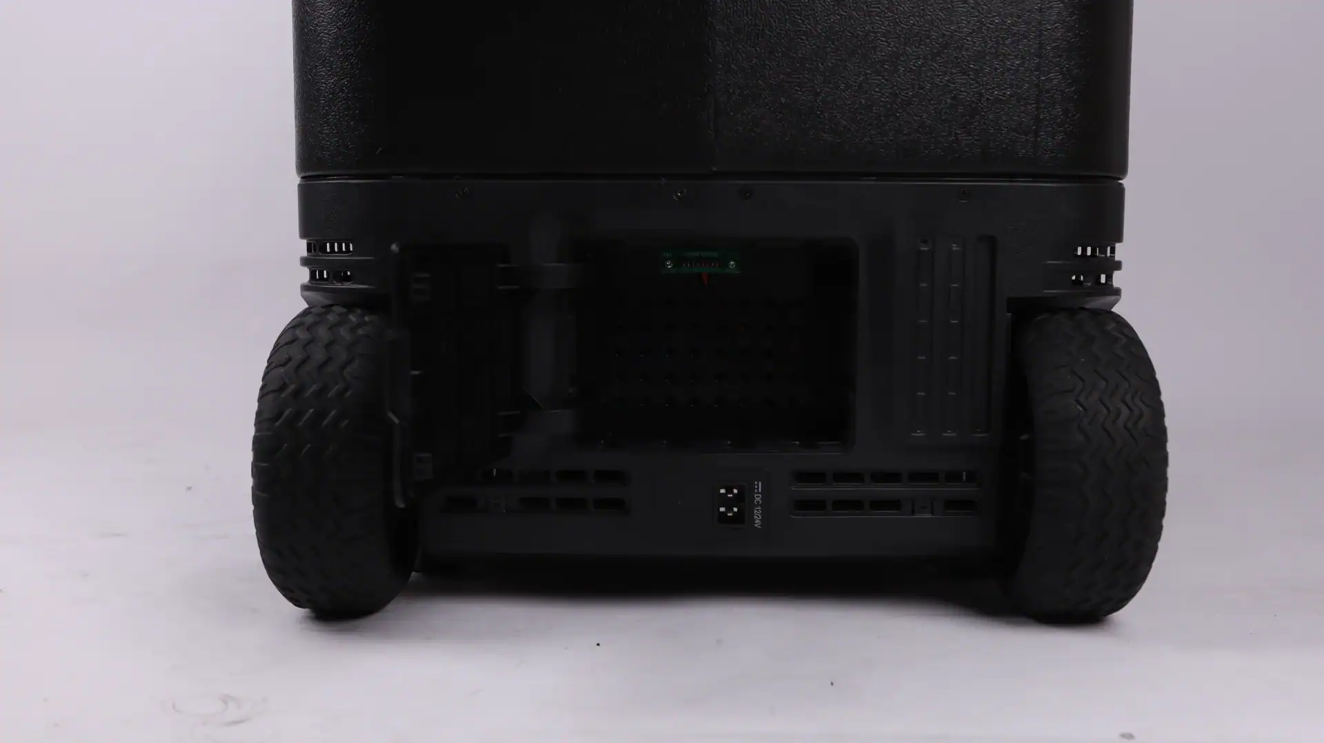Close-up of a black portable storage unit featuring large treaded wheels, a visible open rear compartment, and a DC input socket.
