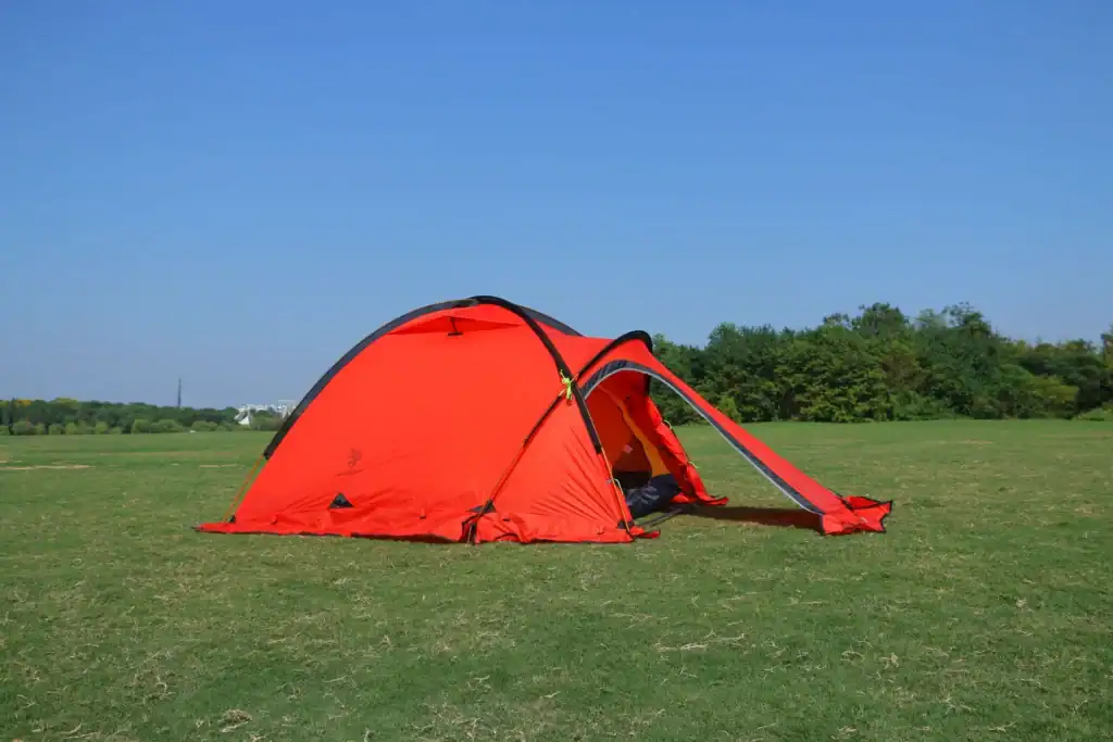 Red camping tent set up on a grassy field under a clear blue sky.