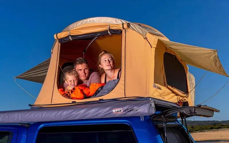 Familienzelten in einem Dachzeltschlafsystem auf einem blauen Auto in natürlicher Umgebung.