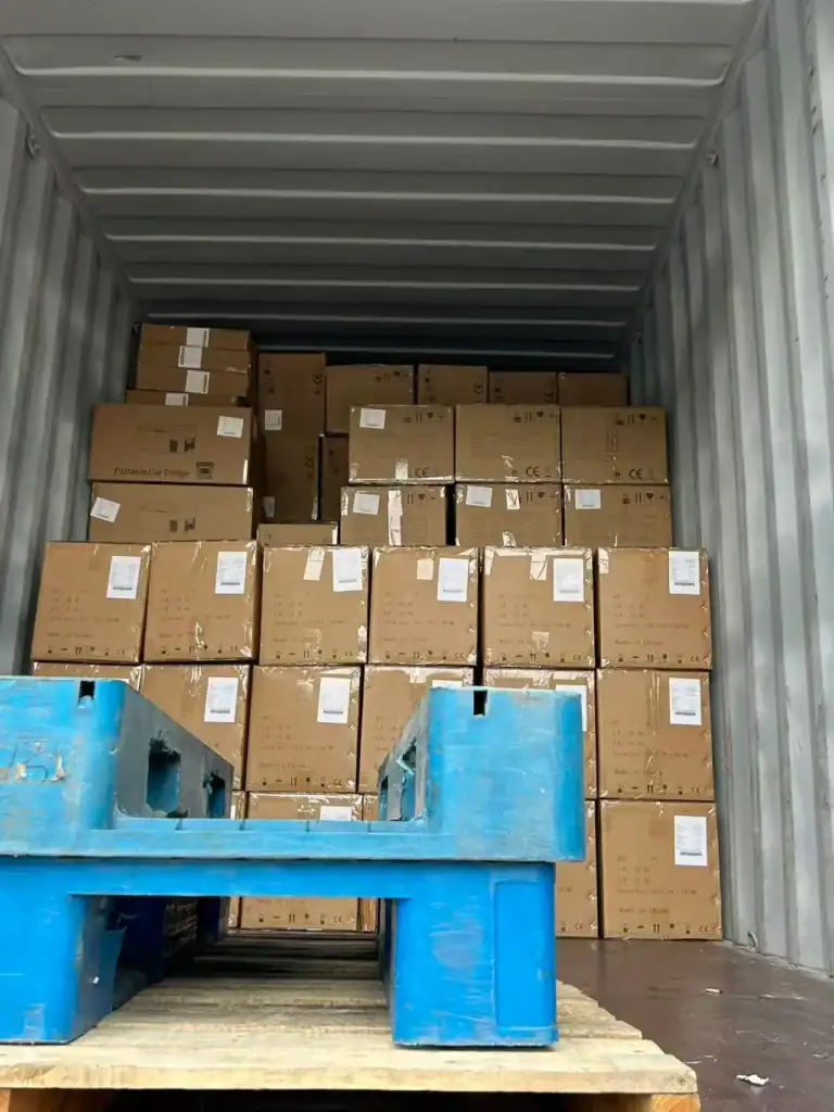 Stacked cardboard boxes labeled 'Portable Car Fridge' arranged inside a shipping container, with a blue pallet in the foreground.