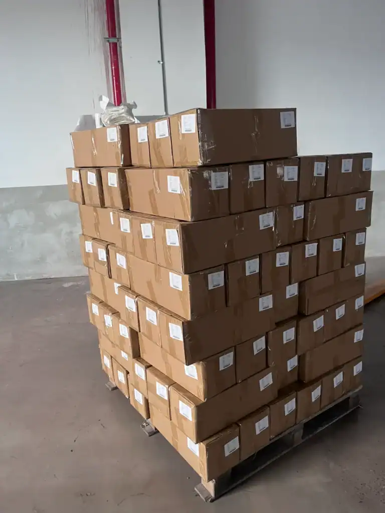 Stacked cardboard boxes labeled and organized on a wooden pallet in a warehouse setting, ready for shipment.