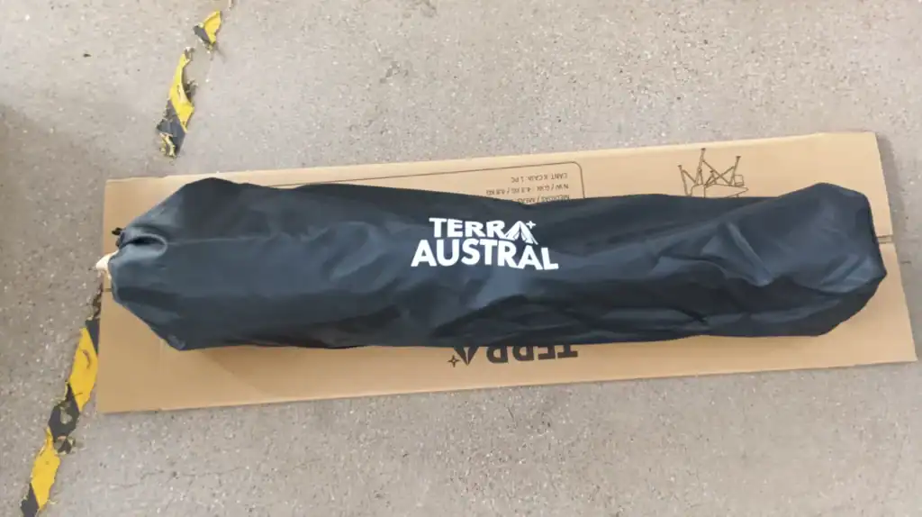 A Terra Austral-branded folding chair packed in a black carry case lying on a cardboard box, placed on a concrete floor.