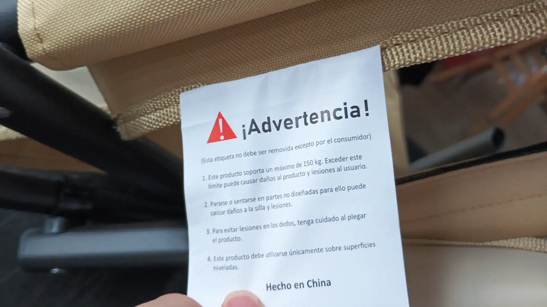 Folding Wagon Weight Limits: Static vs Dynamic Capacity 15 Close-up of a warning label attached to a beige folding chair frame, providing weight and usage instructions in Spanish.