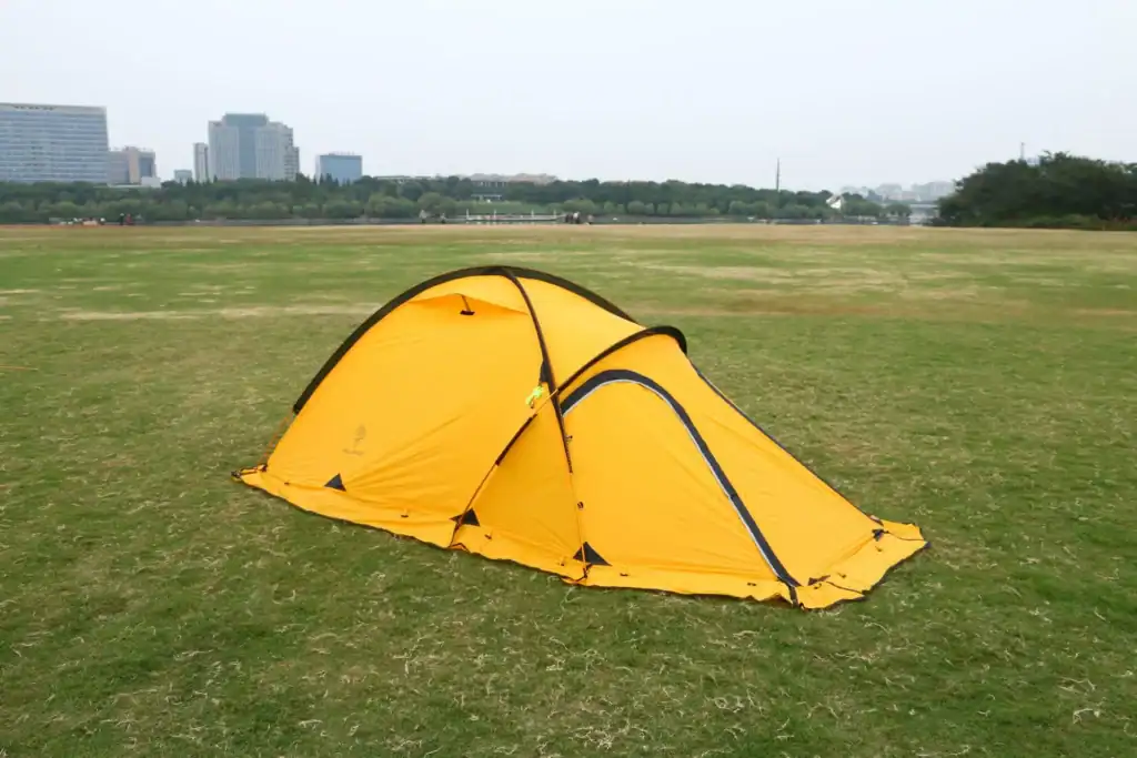 2-Person Ultralight Tent: 5 Ways Floors Fail in Bulk 1 Yellow camping tent set up on a grassy field with city skyline in background.