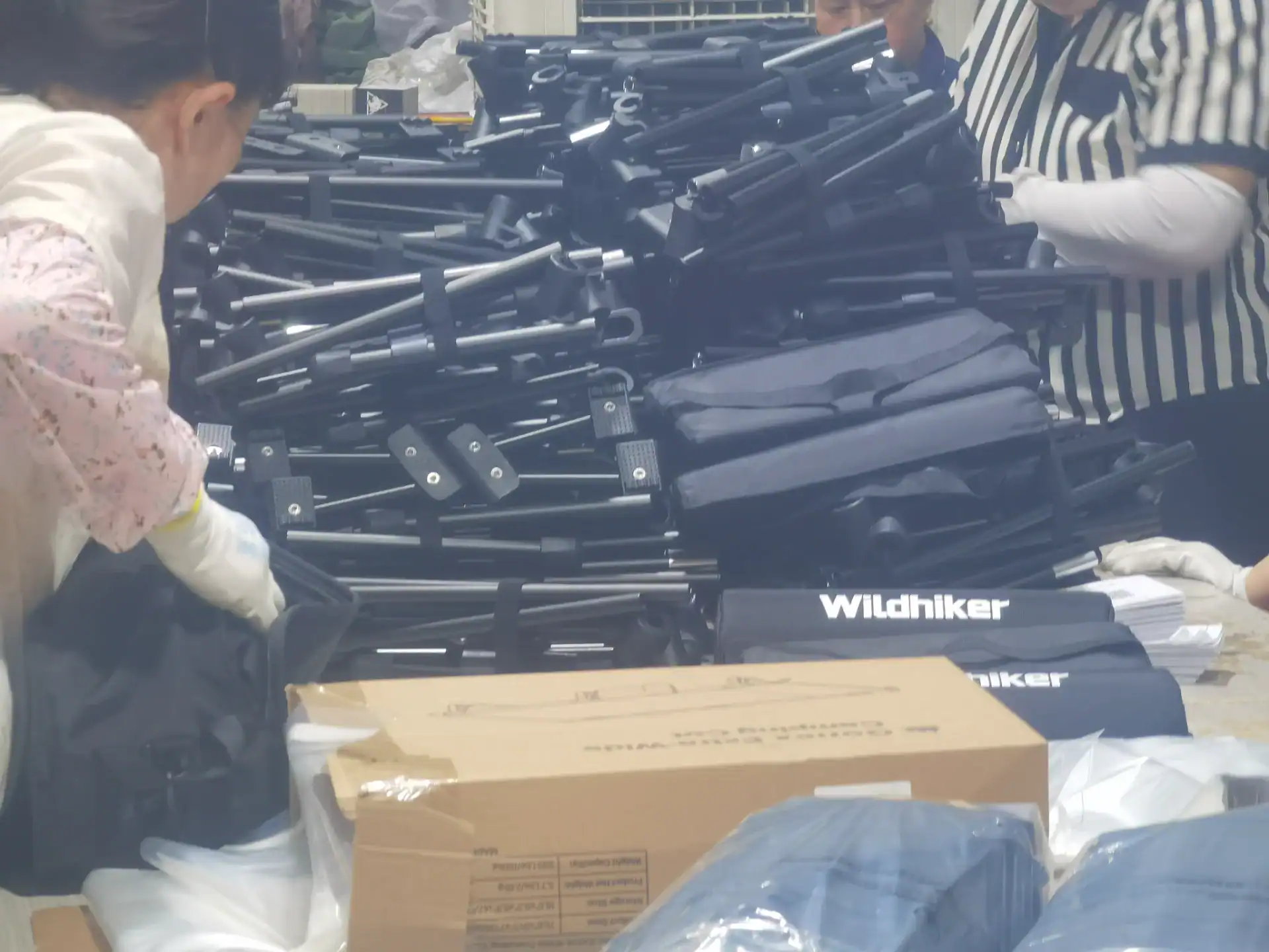 Workers inspecting and assembling folding outdoor chairs with black frames and branded fabric segments labeled 'Wildhiker.'