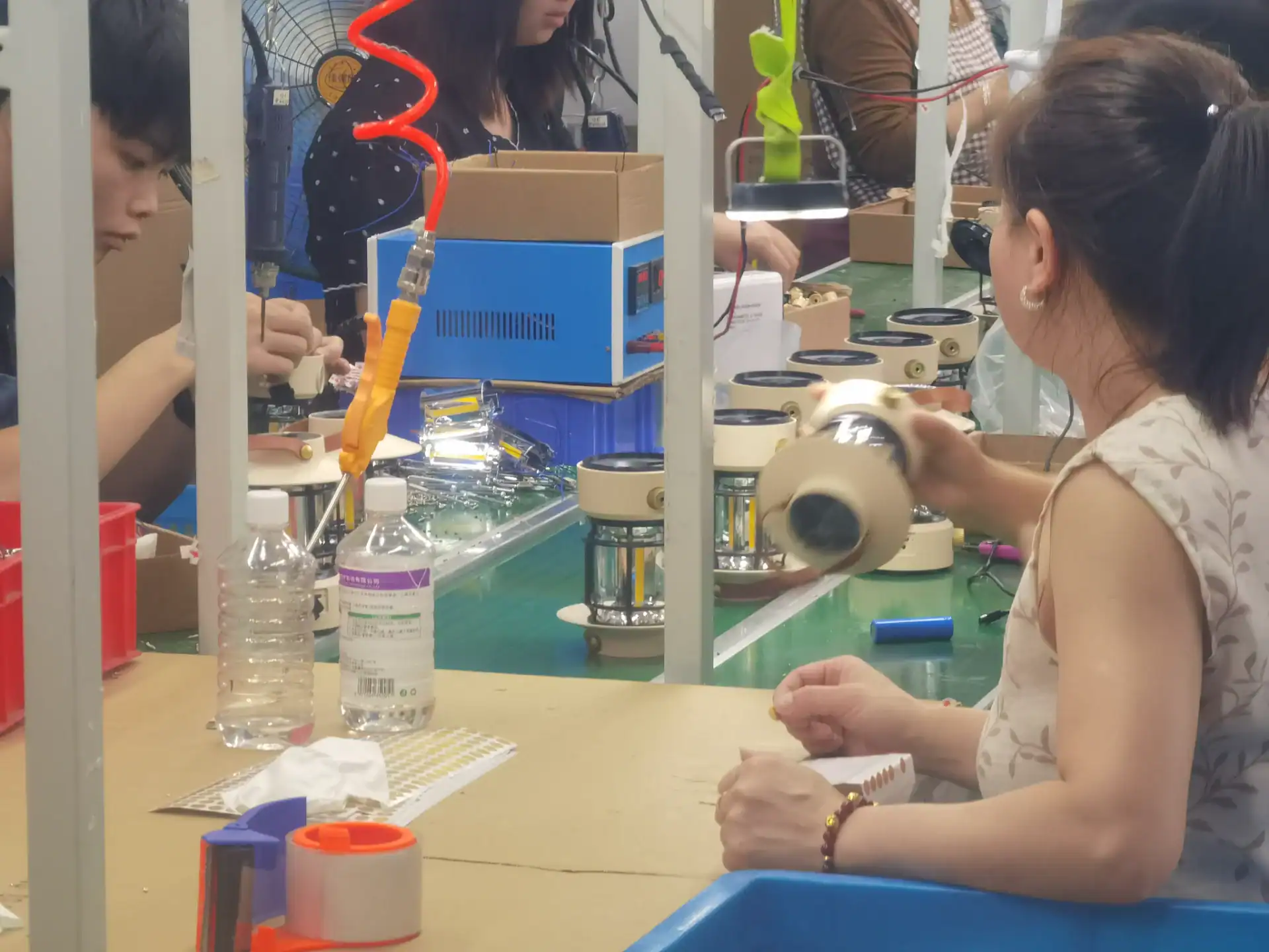 Inflatable Tent Manufacturer Audit: Seams, Valves & Tubes 131 Factory workers assembling products on an assembly line with tools, parts, and packaging materials visible in the workspace.