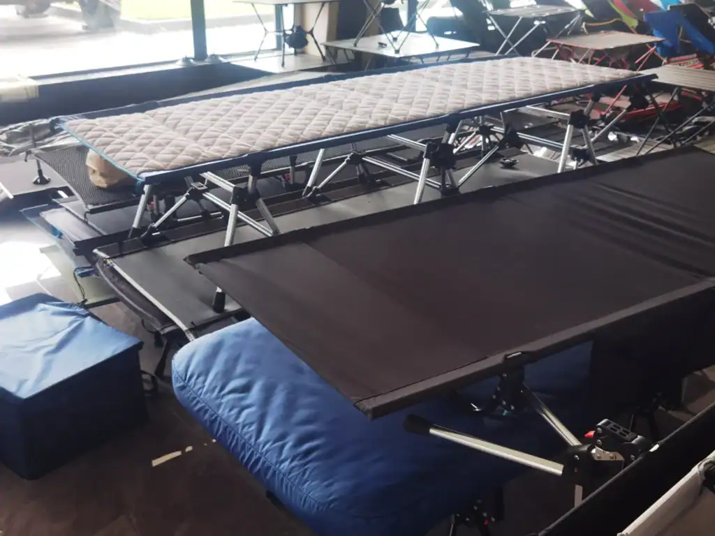 Multiple camping cots with padded and fabric surfaces displayed in a showroom, showcasing diverse designs and features.