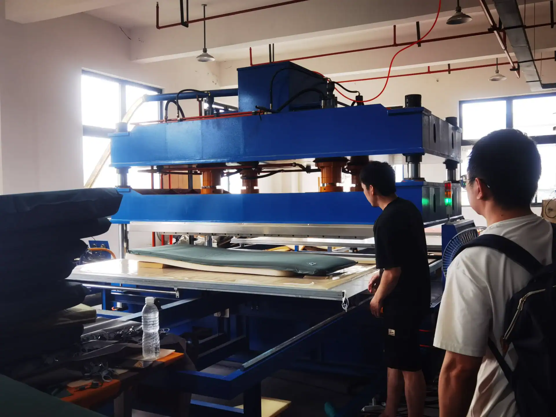 Sourcing Camping Gear: 5 Mistakes That Kill Your Margin 23 Two workers operating a large machine in a well-lit factory during the manufacturing process of camping gear.