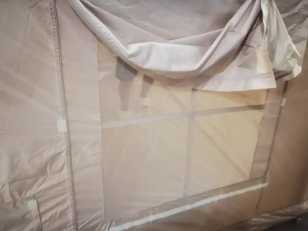 Close-up view of a camping tent wall featuring a rectangular mesh window with a rolled-up fabric cover and Velcro attachments.