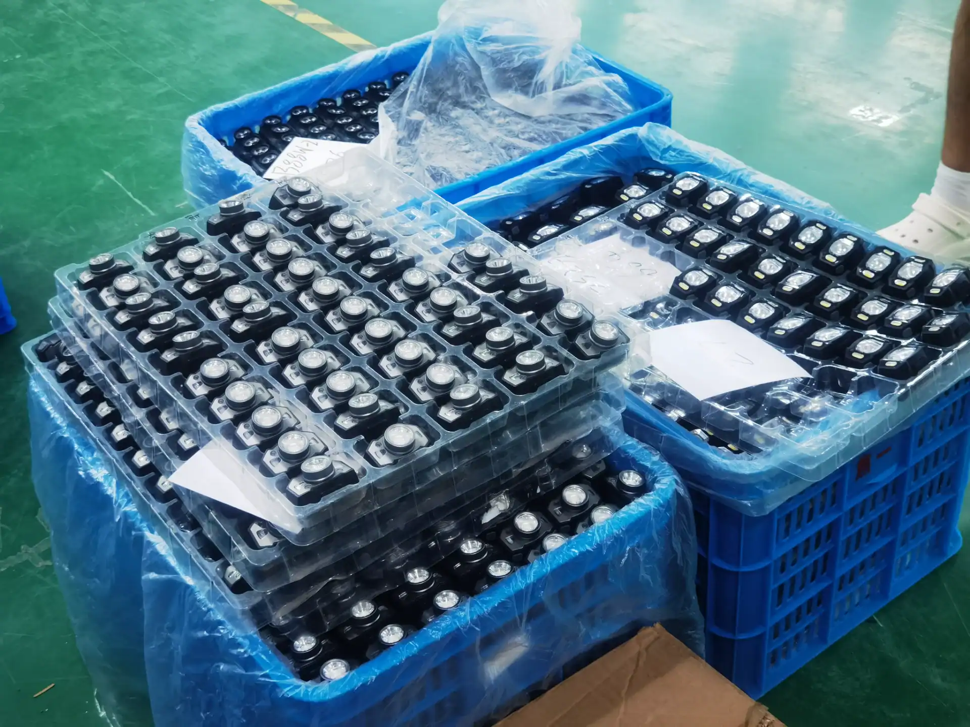 Multiple packaged LED headlamps neatly arranged in transparent trays inside blue shipping crates, ready for distribution.