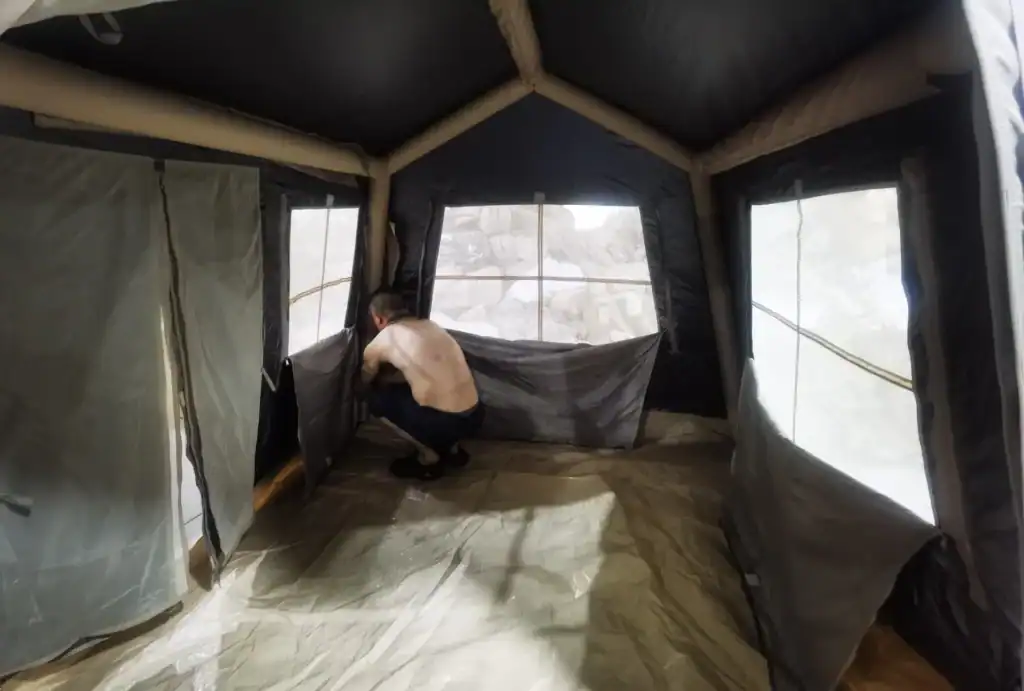 Individual inside a spacious camping tent with fabric walls and windows, arranging interior features in a well-lit environment.
