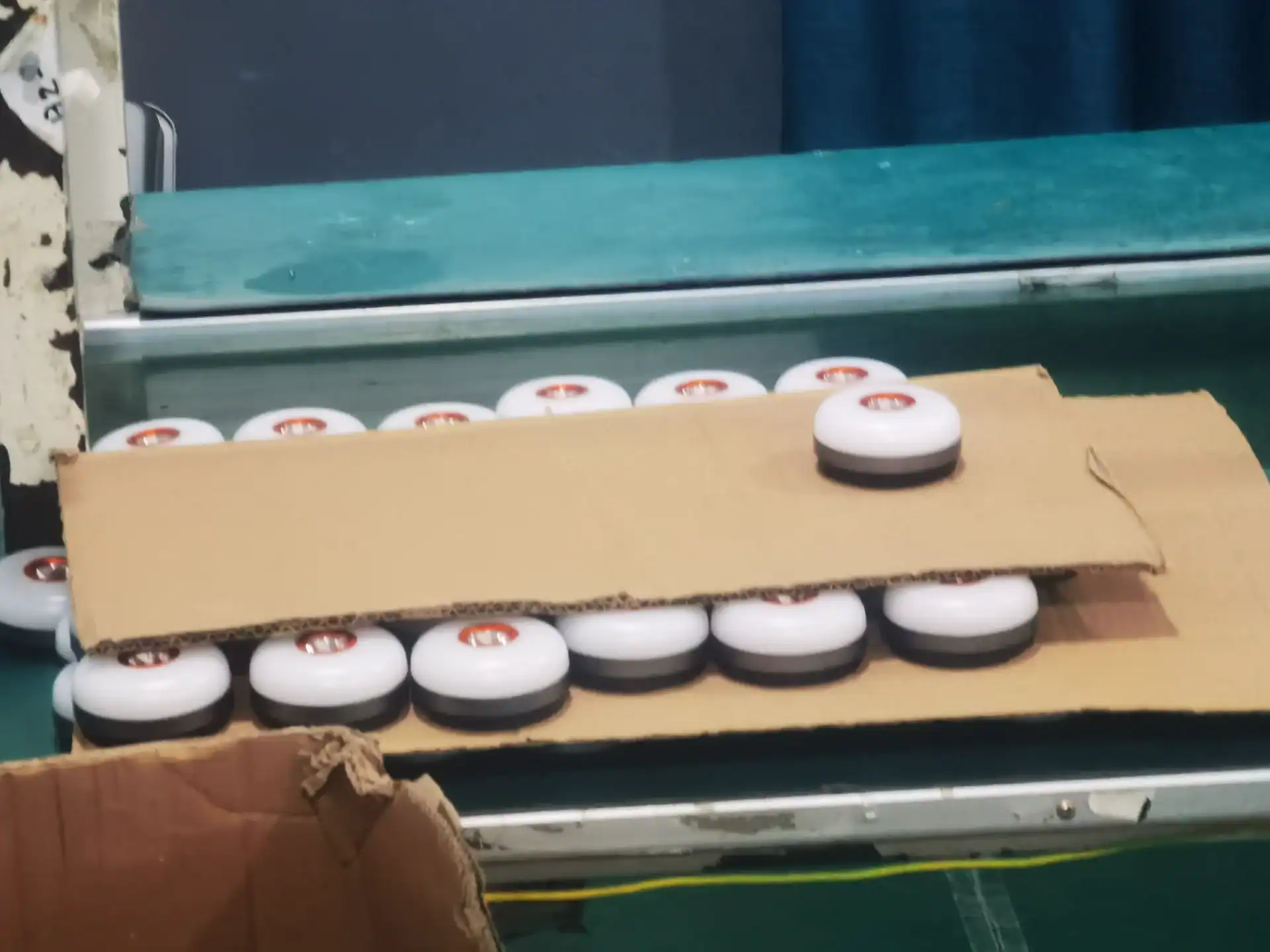 Inflatable Tent Manufacturer Audit: Seams, Valves & Tubes 139 Multiple round LED lights with white tops and black bases stacked between cardboard sheets on a packaging table.
