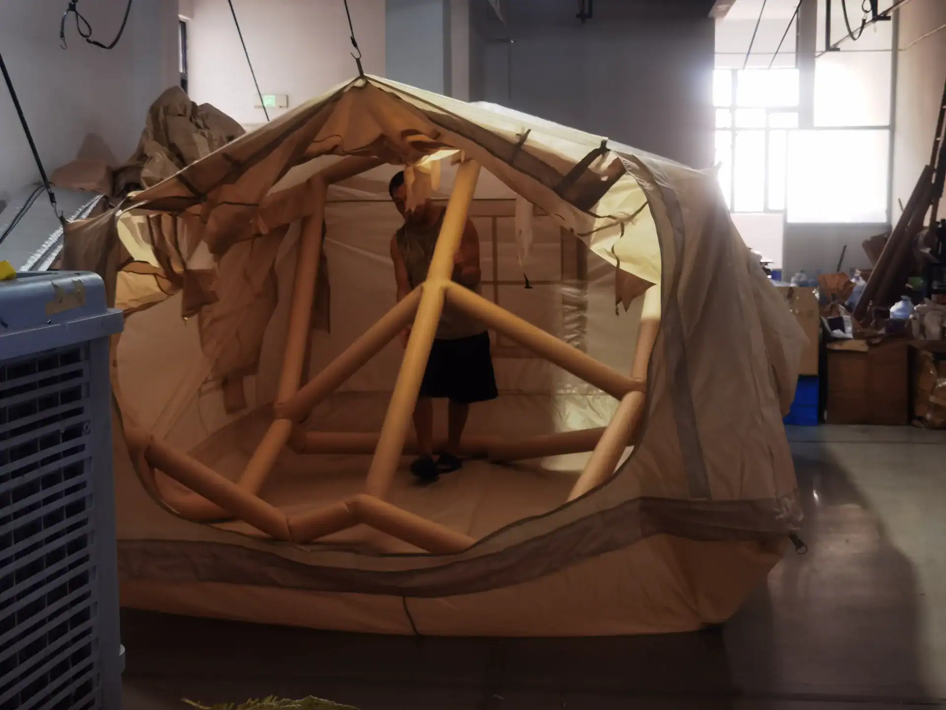 A person testing the structure of an inflatable tent in a workshop, showcasing durable airbeam construction under indoor lighting.