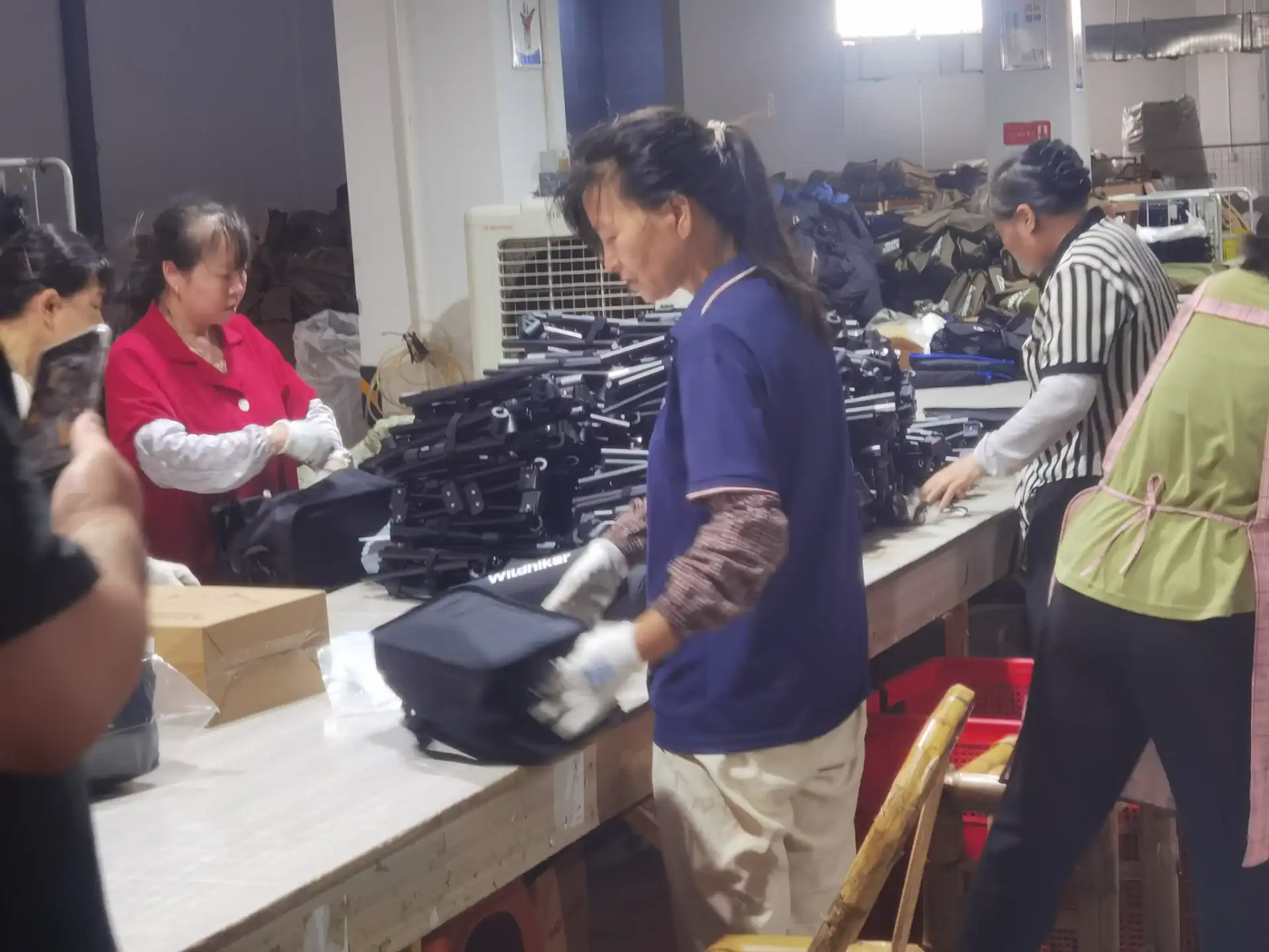 Sourcing Camping Gear: 5 Mistakes That Kill Your Margin 24 Group of workers assembling and inspecting outdoor gear at a factory workstation with equipment and materials on tables.