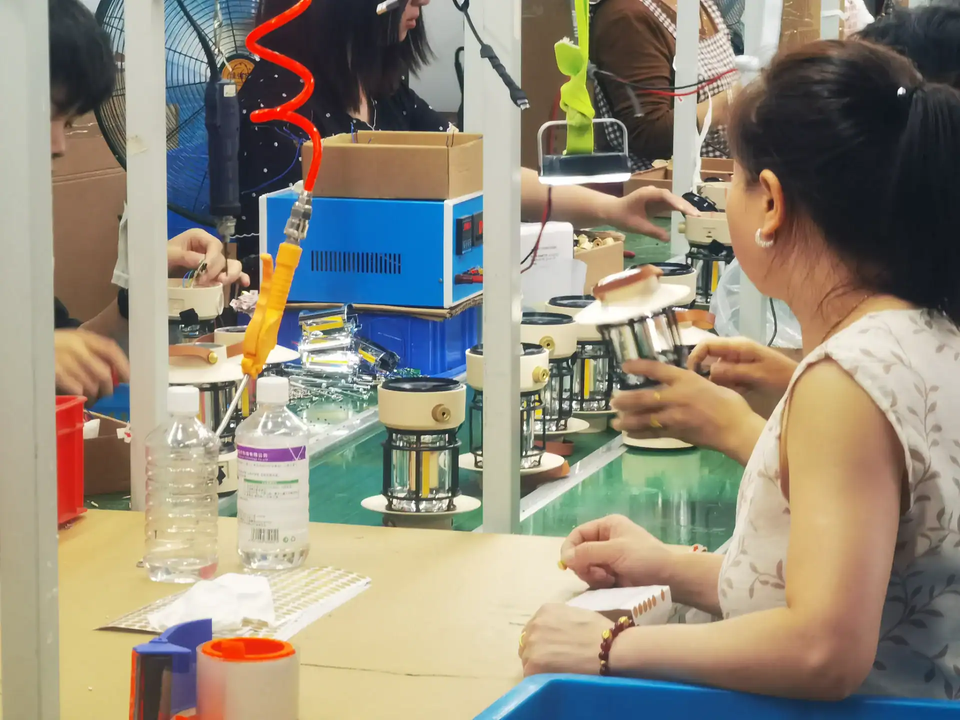 Inflatable Tent Manufacturer Audit: Seams, Valves & Tubes 151 Factory workers assembling products with tools at a workstation, surrounded by materials and equipment in a production line.